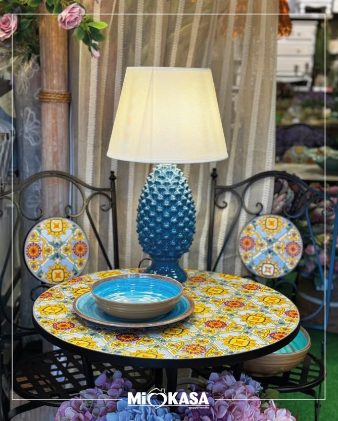 Tavolino in maiolica siciliana con lampada a pigna blu, piatti coordinati e centrotavola di fiori artificiali