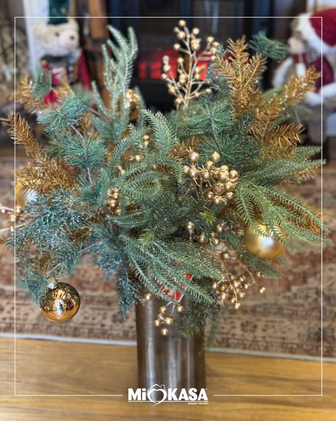 Composizione natalizia con rami di pino innevati, decorazioni e bacche oro in vaso bronzo
